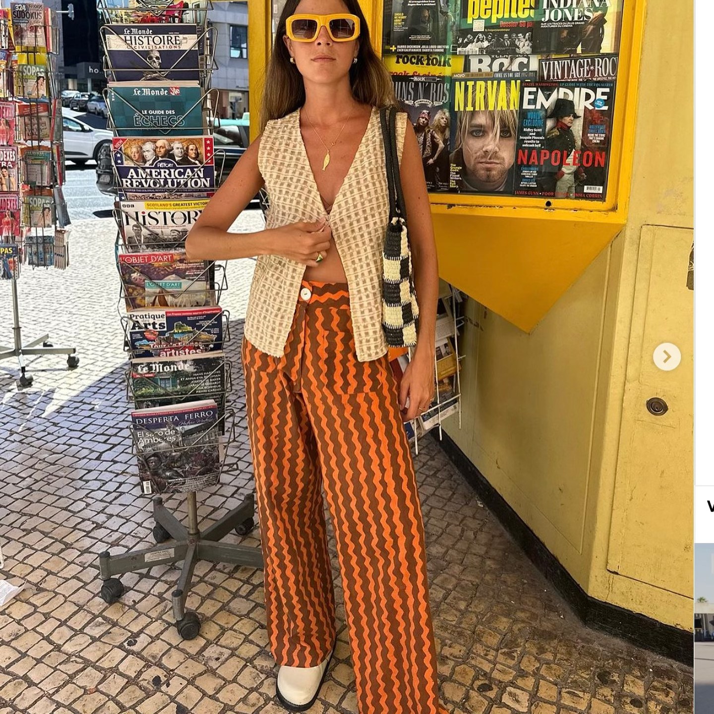 Foto de mulher com calca laranja estampada, óculos de sol e blusa texturizada. Demonstração da moda portuguesa.