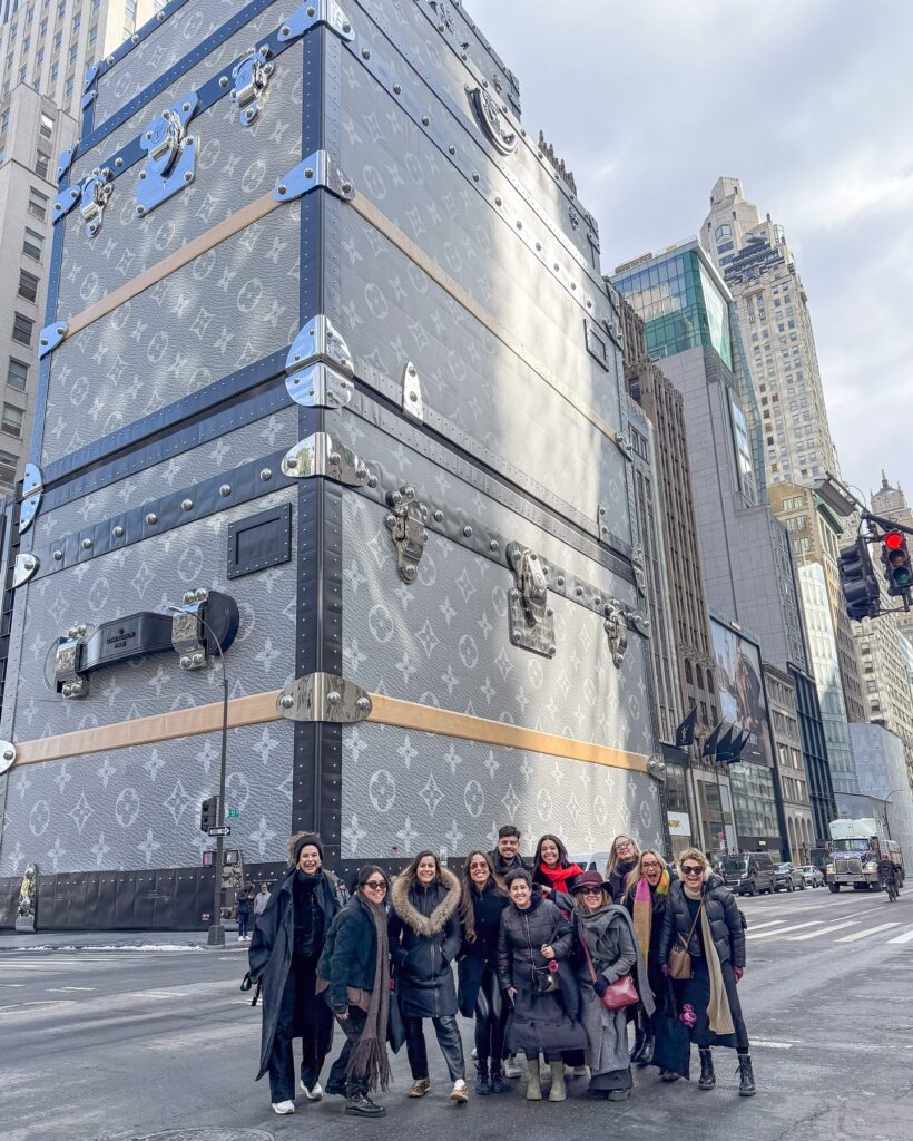 Foto da turma do NY Fashion Tour em frente a loja da Louis Vuitton formada por duas grandes malas da marca. Essa é uma das tendências de varejo e visual merchandisign observadas em Nova York.