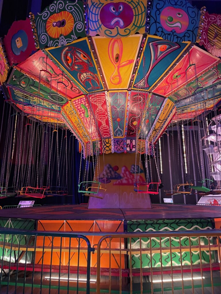 Imagem do brinquedo chapeu mexicano na exposição "Luna Luna: Forgotten Fantasy". O brinquedo do parque é toda pintado com elementos abstratos e iluminação que destaca suas pinturas.
