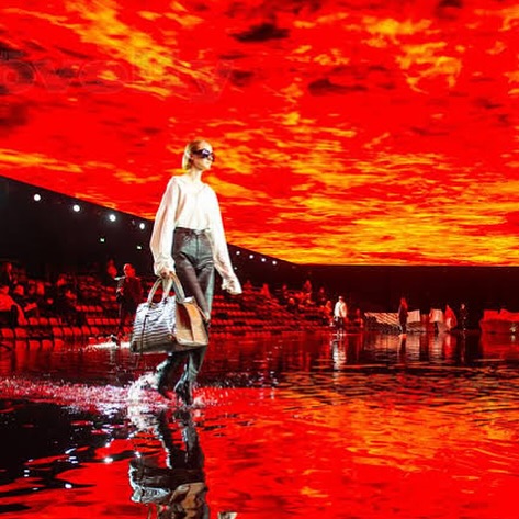 Foto do desfile da Balenciaga pelo estilista Demna Gvasalia em fevereiro de 2020. Na foto, vemos uma modelo na passarela com fogo no teto e piso cheio de água