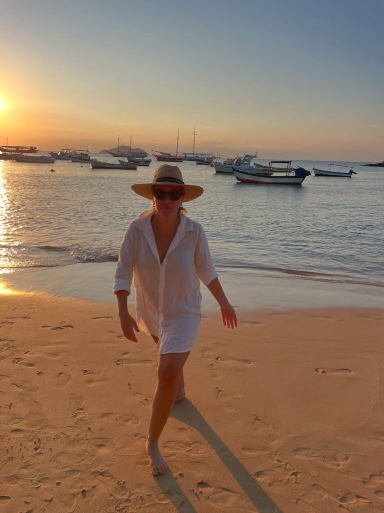 Foto da Silvia em frente ao mar com camisão e chapeu de palha no inverno