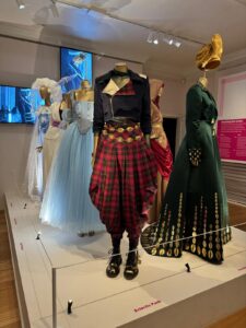 Foto de uma das exposições de luxo em Londres, a Dress Code. A foto mostra diferentes trajes femininos de figuras públicas que representam o luxo.