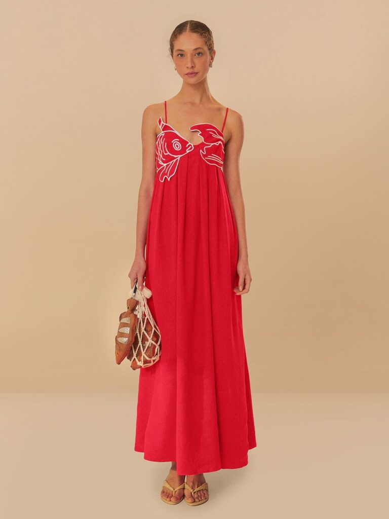 Modelo vestindo vestido laranja com uma sardinha costurada em linha branco no busto. 