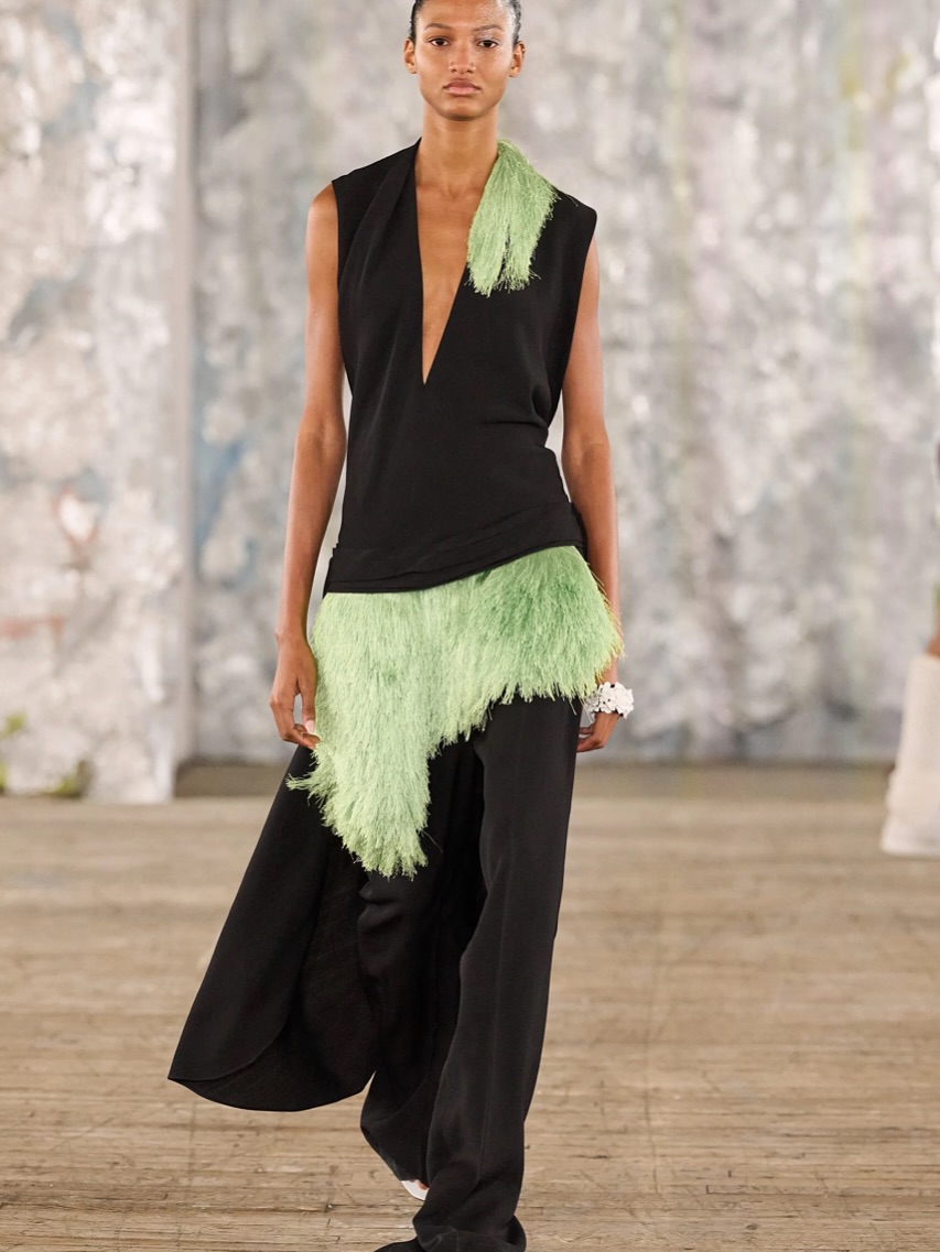 Modelo usa calça de corte largo com cintura baixa e colete, ambos em cor preta.