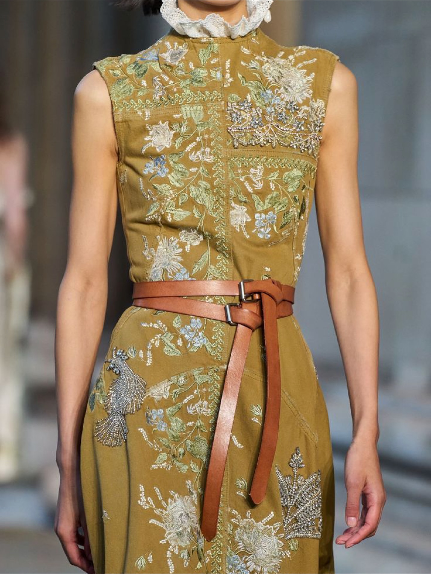 Foto de modelo utilizando vestido verde e dois cintos marrons com pontas em destaque.